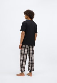 Tricou negru din bumbac asociat cu pantaloni de pijama cu carouri, cu culori negre, maro și albe. Pantalonii au un brâu elastic și mansete.