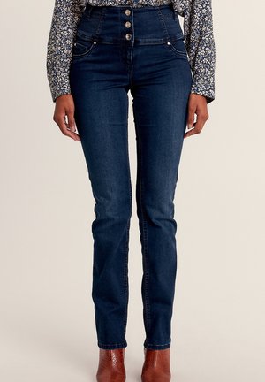 Hoge taille, donkerblauwe skinny jeans met vijf knopen, lichte stiksels en voorkant zakken, gecombineerd met een geblokte top en bruine laarzen.