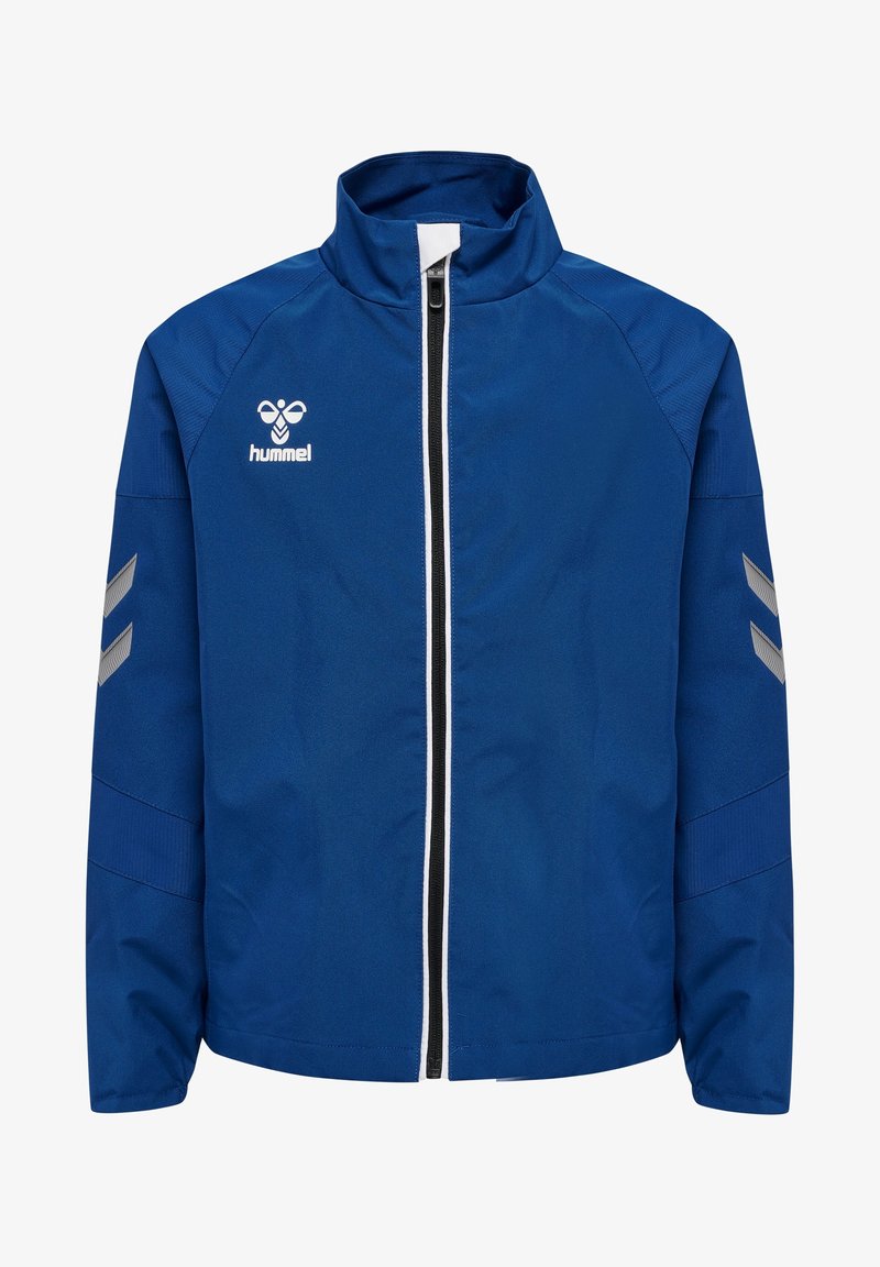 Veste de sport bleue avec fermeture éclair complète à l'avant, bordure de fermeture éclair blanche et noire, chevrons réfléchissants sur les manches, et logo blanc hummel sur la poitrine.