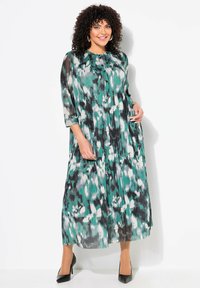 Robe longue plissée en teinte bleu canard, avec un motif floral noir et blanc. Elle présente un devant à boutons, des manches trois-quarts et des poches sur les côtés.