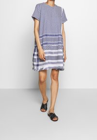 Kjol med kort ärm och knälängd i marinblå och vit med geometriska mönster, med en lös passform och rund halsringning. Lättviktig tyg.