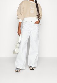 Beige kort sweatshirtdress med vita manschetter, prydd med blommig brodyr framtill; kombinerad med lösa vita jeans och grå sneakers.