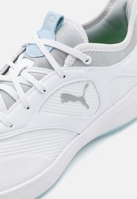 Baskets blanches avec des accents gris, en matériau en maille texturée, et un onglet bleu. Équipées de lacets blancs et d'un logo Puma argenté sur le côté.