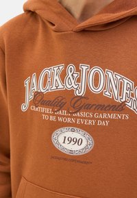 Brown hoodie made of soft fabric featuring a large white logo with "JACK & JONES" and "Quality Garments" text, and a circular 1990 detail.