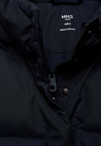 Mörkblå vattenavvisande jacka inuti med dragkedja och tryckknappsstängning, har en etikett som visar storlek S, samt materialets textur.