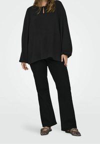 Camiseta negra de manga larga con detalle de ojal, combinada con pantalones negros acampanados y zapatos de casa con estampado animal. Tejido suave, ajuste relajado.