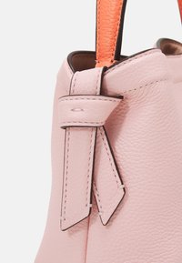 Borsa in pelle rosa chiaro con superficie strutturata, caratterizzata da una maniglia arancione e un dettaglio decorativo sulla cinghia. Forma compatta e strutturata.