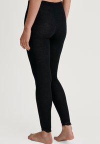 Leggings neri a coste con cintura alta e pizzo alla caviglia, realizzati in un materiale morbido ed elastico. Modello a piedi nudi.