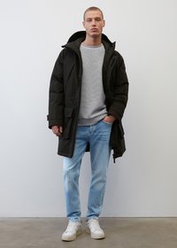 Schwarze Puffjacke mit Kapuze und Fronttaschen, getragen über einem grauen Sweatshirt und hellblauen Jeans. Weiße Sneakers mit strukturiertem Sohlen.