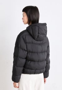 Melna pūkaina jaka ar kapuci, ar quilted dizainu un mīkstu tekstūru. Īsa, brīva piegriezuma ar elastīgiem manžetēm.