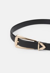 Cinturón de cuero negro con hebilla de metal dorado que presenta una forma triangular única y dos aberturas para presionar como orificios de ajuste.