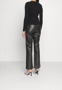 Svart ribbat långärmat top som är kombinerad med högmidjade svarta läderbyxor och silverfärgade sandaletter, sedd bakifrån.