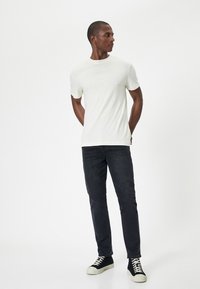 Ljus beige kortärmad t-shirt i kombination med mörka jeans och svarta högstövlar med vita sulor. Enkelt, figursytt design; mjuk textur.