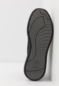 Sole di scarpa sportiva nera, caratterizzata da una superficie in gomma grigia texturizzata con un motivo a onde e battistrada triangolare per la presa. Branding sottile visibile.