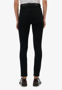 Jeans skinny de mezclilla negra con una cintura alta, que cuentan con dos bolsillos traseros y una textura suave, combinados con zapatos oscuros de cordones.