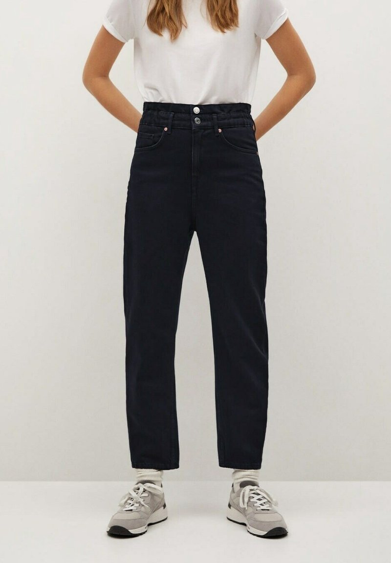 Jean en denim foncé taille haute avec une taille froncée, des boutons à l'avant et une coupe décontractée. Associé à un t-shirt blanc uni et des baskets.