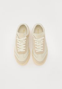Beige sneakers med en blanding av semsket skinn og glatt lær, med hvite lisser og en lys brun gummisåle. Diskret logo detaljer på tungen.