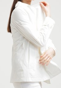 Vit lättviktsjacka med rak passform, knäppning framtill och sidfickor. Slät textur med en fräsch krage detaljer.