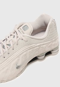 Lys grå Nike træningssko med en struktureret overflade, mesh-krave og polstret tungespids. Har sølv detaljer og mønstret sål med synlige luftkamre.