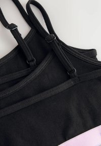 Két fekete szövetből készült rövid felső állítható pántokkal, egymásra fektetve egy fehér felületen.