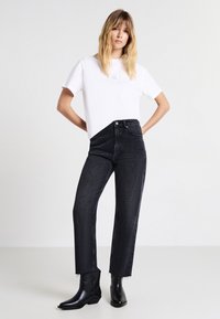 Pantaloni in denim neri a vita alta con orlo sfilacciato, abbinati a una T-shirt in cotone bianca con una grafica centrata e stivaletti neri alla caviglia.