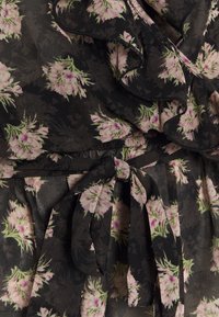 Robe noire à motifs floraux avec des fleurs roses et vertes, bordures volantées et ceinture nouée à la taille. Confectionnée dans un tissu léger et texturé.