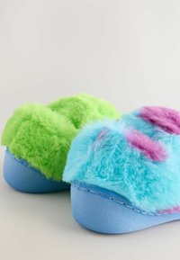 Flauschige Hausschuhe aus leuchtend grünem und blauem Plüschmaterial mit rosa Akzenten, auf einer soliden blauen Stoffsohle montiert.