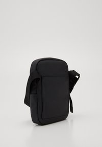 Crni platneni crossbody torba pravokutnog oblika, teksturirane površine, s podesivim remenom i prednjim džepom za dodatno pohranu.