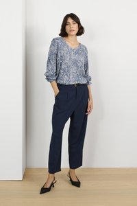Chemisier à manches longues à motifs bleus avec un col en V, associé à un pantalon taille haute bleu marine et des escarpins à bout pointu noirs.