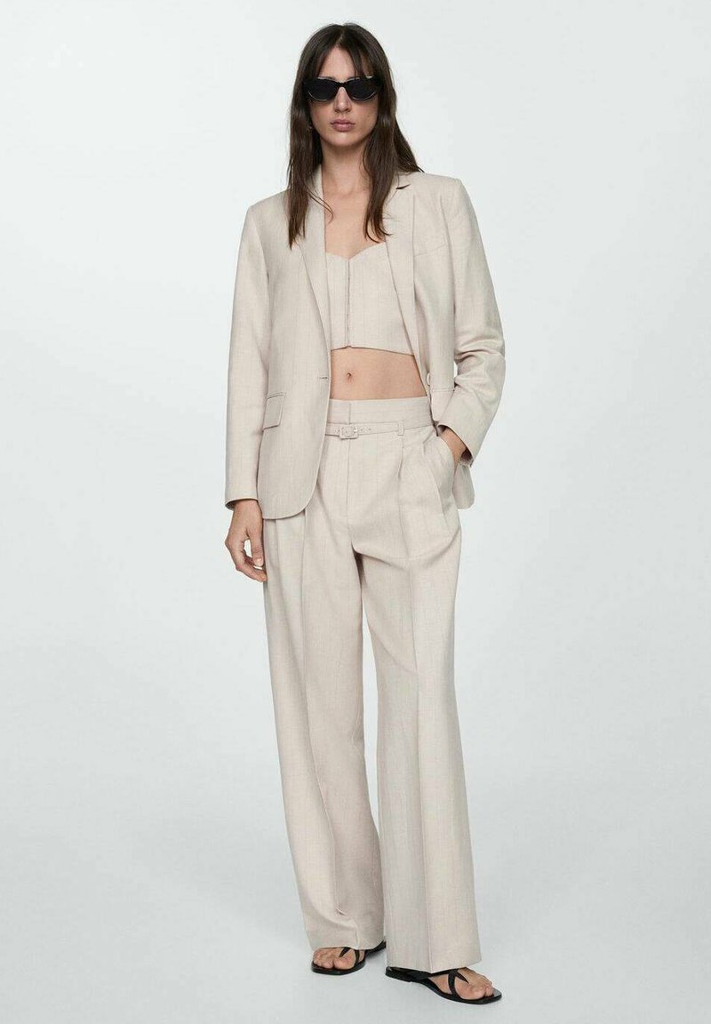 Beige Leinenanzug mit einem bauchfreien Oberteil und weit geschnittenen Hosen. Sanfte Textur, Blazer mit einem Knopf und elegantes, minimales Design.