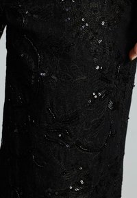 Tessuto in denim nero con ricami floreali intricati, caratterizzato da paillettes e perline per texture e dettagli. Inquadratura ravvicinata del capo.