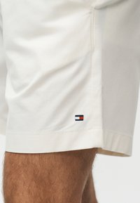 Κοντό λευκό σορτς σε έναν άνθρωπο, με μικρό κεντημένο κόκκινο, λευκό και μπλε σημαία κοντά στο τελείωμα.