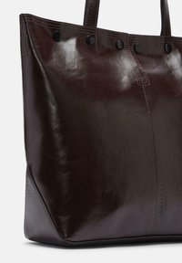 Brązowa skórzana torba na ramię o połyskującym wykończeniu, z haftowanym wzorem, czarnymi zatrzaskami i uporządkowanym prostokątnym kształtem.