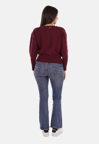Maglione a collo ampio di colore bordeaux, con orlo a coste, abbinato a jeans a zampa d'elefante blu, dotati di tasche posteriori, e sneakers bianche.