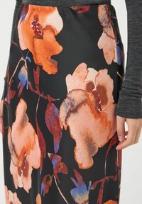 Falda de tela con estampado floral en negro con grandes flores naranjas y azules. El material parece suave con un ligero brillo.