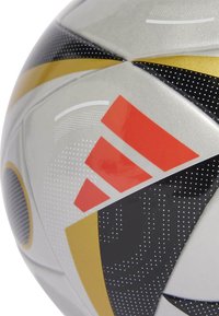 Close-up srebrno-crno-zlatnog panela nogometne lopte s crvenim Adidas logotipom i točkastim uzorcima.