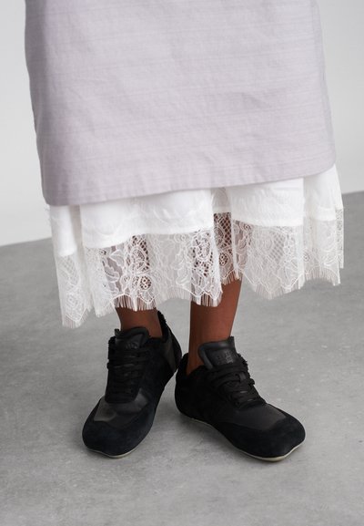 Siva lanena suknja slojevita preko bijelog čipkastog ruba, u paru s crnim sued kožnim tenisicama s kožnim naglascima i teksturiranim gornjim dijelom.