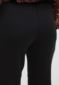 Zwarte elastische broek met een gladde textuur, voorzien van een hoge taille en een eenvoudig ontwerp, gecombineerd met een patroon top in warme tonen.