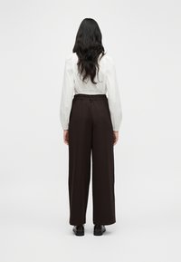 Καφέ παντελόνι φαρδύ με ελασ τική μέση, σε συνδυασμό με λευκό, μακρυμάνικο πουκάμισο με φουσκωτά μανίκια. Ομαλή υφή υφάσματος.