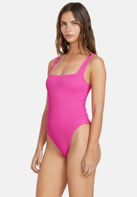 Maillot de bain une pièce rose avec une texture côtelée, décolleté carré et bretelles larges, présentant des jambes hautes pour une silhouette élancée.