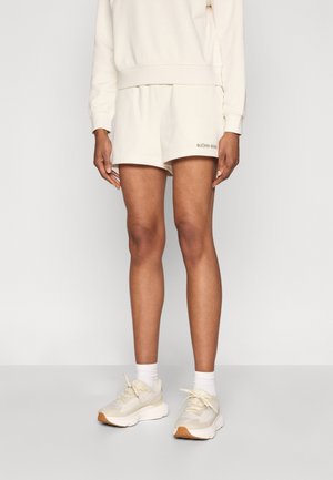 Sweatshirt i cremefarve med ribstrikkede manchetter, kombineret med matchende cremefarvede shorts. Indeholder printet logo og letvægtsstof. Hvide sportssko fuldender looket.