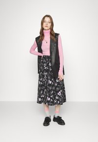 Saia midi preta com flores roxas, suéter cor-de-rosa de gola alta e um colete de couro preto sem mangas, acompanhado de sapatos pretos e meias às riscas.