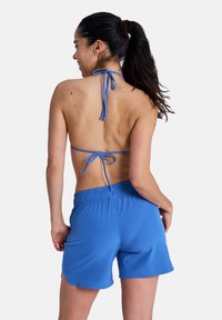Ανοιχτό μπλε μπικίνι με δέσιμο χαλτέρ στον λαιμό και ανοιχτή πλάτη. Διαθέτει σορτς με ελαστική μέση, λείο ύφασμα και διακριτικές λεπτομέρειες ραφής.