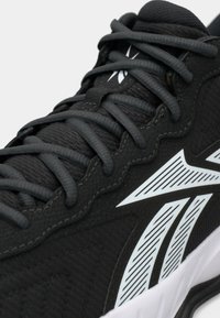 Zapatilla deportiva negra con parte superior texturizada, cordones a juego y acento del logotipo blanco. Presenta una suela acolchada y detalles de costura suave.