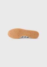 Shoe sole with a gum rubber material, featuring circular traction patterns and three black stripes on a white background.