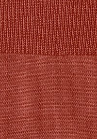 Nahaufnahme eines strukturierten Stoffes in einem warmen rötlich-braunen Farbton, der ein geripptes Muster und sanfte Übergänge zwischen zwei Bereichen zeigt.