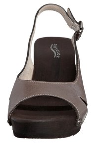 Sandale en cuir marron avec ouverture à l'avant et bride autour de la cheville. Semelle en bois avec un léger talon. Présente un design découpé incurvé et des coutures contrastantes.