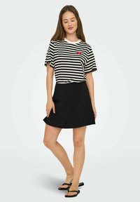 Falda negra combinada con una camisa de manga corta a rayas en blanco y negro que presenta un logo rojo. La tela parece suave, con elementos de diseño simples.