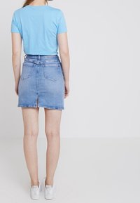 Blå bomullströja i kombination med en ljusblå jeanskort som går till knäna och har en sprund bak, bärs med vita sneakers.