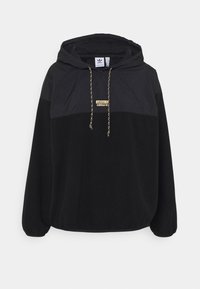 Černá mikina s kapucí, klokaní kapsou, stahovací šňůrkou na kapuci a texturovaným horním panelem. Na hrudi zlatý detail loga. Měkká látka.